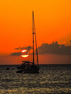 Jolly Sienda Prints: Seven Mile Beach, Grand Cayman. Sailboat and a boat with the orange sun setting behind