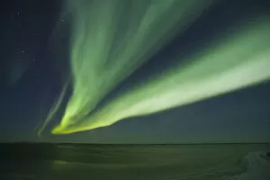 Shimmering curtains of green Aurora borealis dance in the southern sky over a lagoon