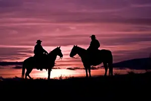 A silhouette of two cowboys on horses with the winter sky on The Hideout Ranch in Shell Wyoming