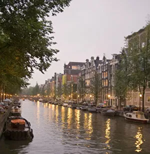 Street lights reflect onto the boat lined canal at dusk