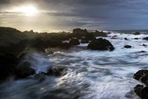 The sun breaks through storm clouds along the California Coast as surf breaks