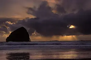 Seastack Prints: Sunset colors the skies as the sun sets behind clouds near on the horizon at Cape Kiwanda