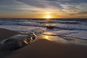 Sunset reflecting off the water on the sand of a beach
