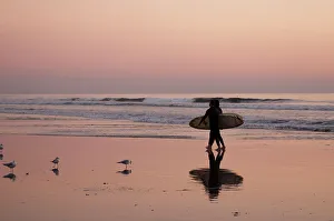Surfing Prints: Surfers cast a shadow on wet sand as they walk on Huntington Beach at sunset