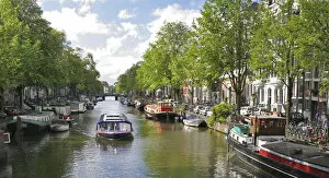 A tour boat passes many colorful houseboats on a tree lined canal
