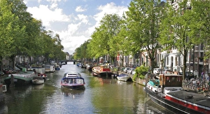 A tour boat passes many colorful houseboats on a tree lined canal A tour boat passes many colorful houseboats on a tree lined canal