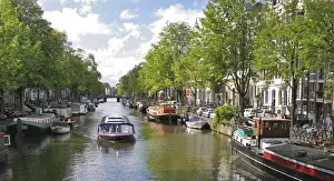 Houseboat Prints: A tour boat passes many colorful houseboats on a tree lined canal