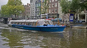 A tour boat full of people travel a canal lined with colorful gabled homes