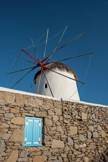 View From Below Prints: A traditional windmill set behind a rock masonry wall