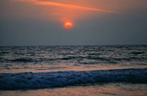 USA, California, Los Angeles Co. The setting sun, muted red, drops into the waves