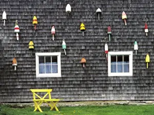 USA, Maine, Boothbay Harbor. Bright buoys decorate the weathered shingles of this