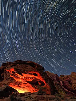 Usa, Nevada. Valley of Fire State Park, star trails and campfire glowing in sandstone rocks