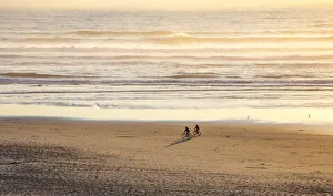 Bicycle Prints: USA, Oregon, Cape Arch with two riding bikes on the beach in the evening light