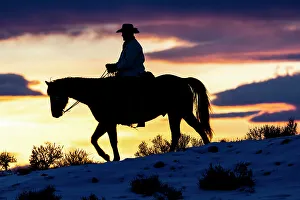 USA, Shell, Wyoming. Hideout Ranch cowboy on horseback silhouetted at sunset. (PR, MR)