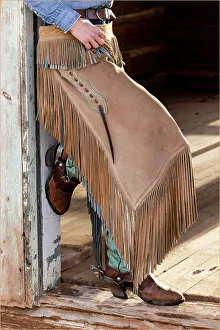 Images Dated 9th June 2022: USA, Shell, Wyoming. Hideout Ranch cowgirl standing in doorway with cowboy boots and chaps