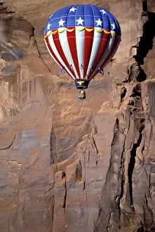 USA, Utah, Monument Valley. A patriotic hot-air balloon floats by a red rock wall