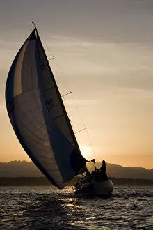 USA, Washington, Seattle, Setting sun lights yacht sailing in Elliot Bay on spring