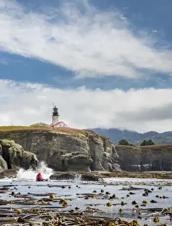 USA, Washington State, Male sea kayaker paddling along cliffs beneath lighthouse