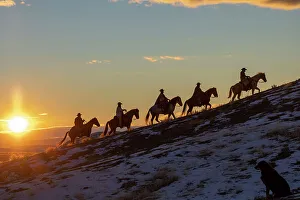 USA, Wyoming. Hideout Horse Ranch, wranglers on horseback in snow at sunset. (MR, PR)