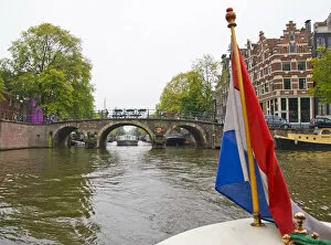 View from the front of a boat with a colorful flag, traveling a canal towards a bridge