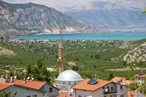 View of Lake Egirdir beyond hilly green land, village mosque with tin dome in front