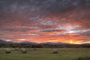 Bale Prints: Vivid sunrise clouds over hay bales in field and the Whitefish Mountain Range in Montana