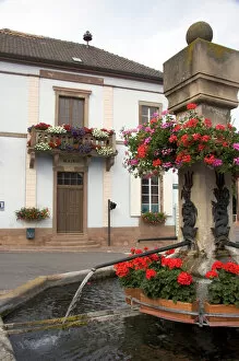 Water fountain with red geraniums in the village of Roschwihr, Eastern France