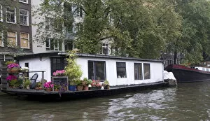 A white houseboat with lots of pink flowers surrounded by trees