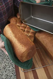 Homemade Prints: Woman removing loaf of just baked multigrain bread from bread pan. (MR)
