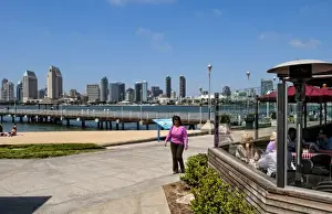 Images Dated 2027: Woman walking on pavement with scenic of skyline of San Diego from Coronado Island