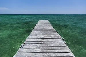 Cuba Prints: A wood dock in the foreground with clear green water and blue skies near the Isle of Youth