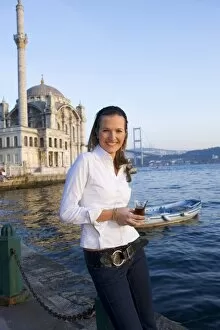 Young woman holding Turkish tea glass, in front of Great Mecidiye Mosque, Ortakoy on the Bosphorus